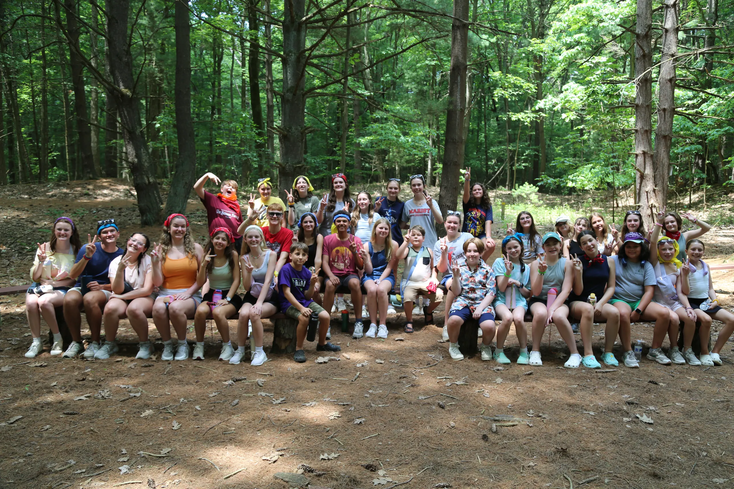 The full camp group seated together on a log bench in the woods