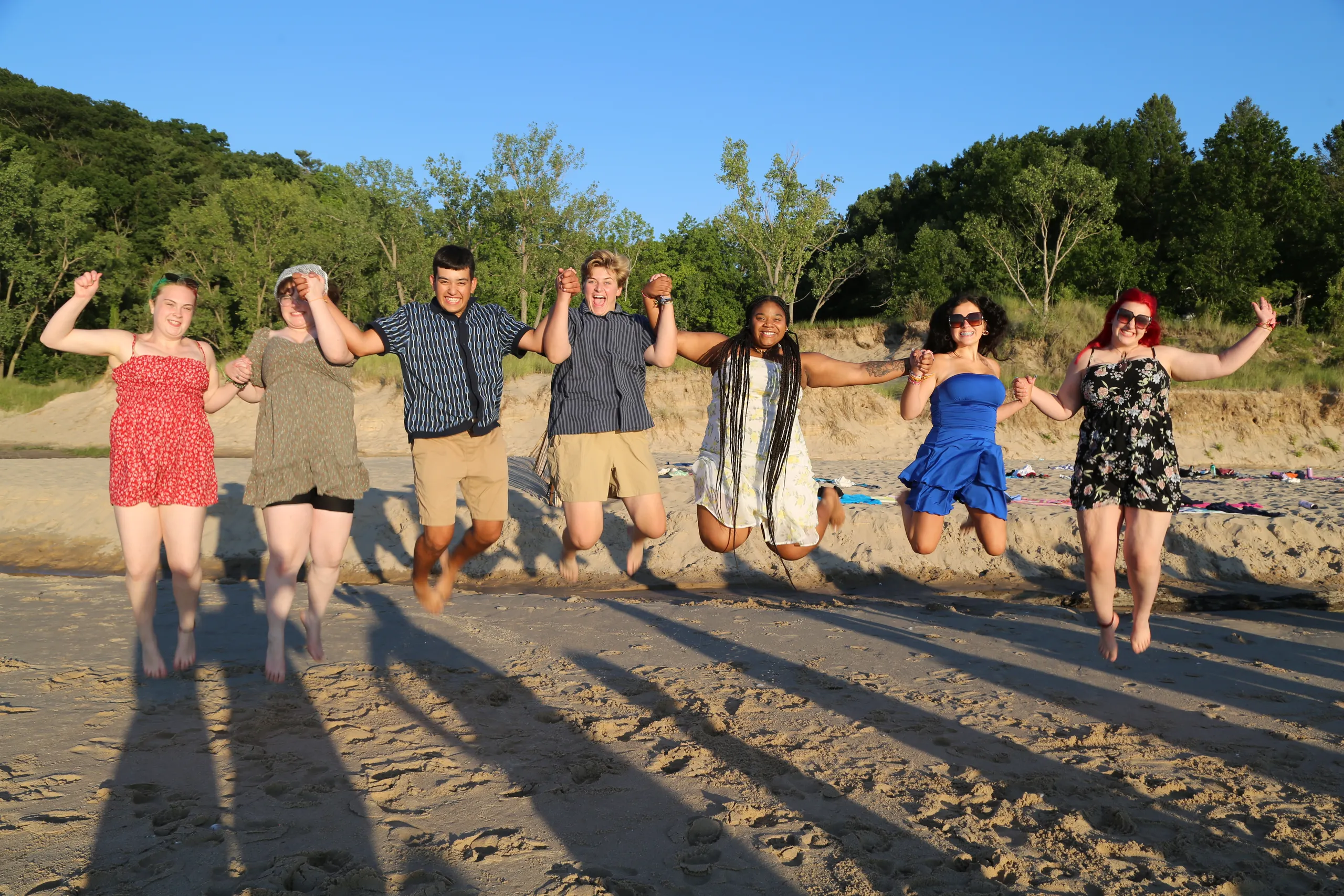 Campers jumping together on the beach at golden hour
