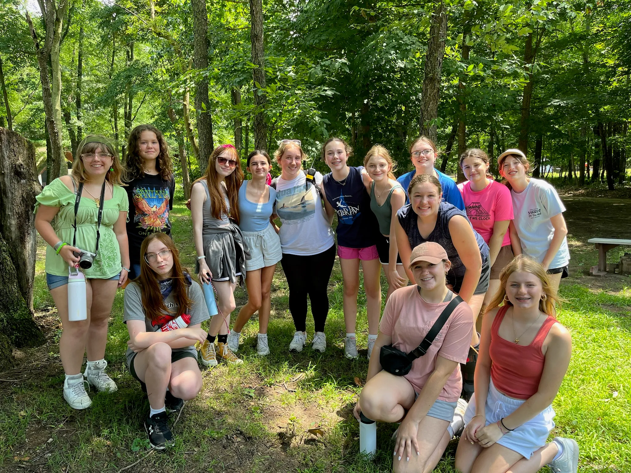 A small group of campers posing together in a sunlit forest clearing