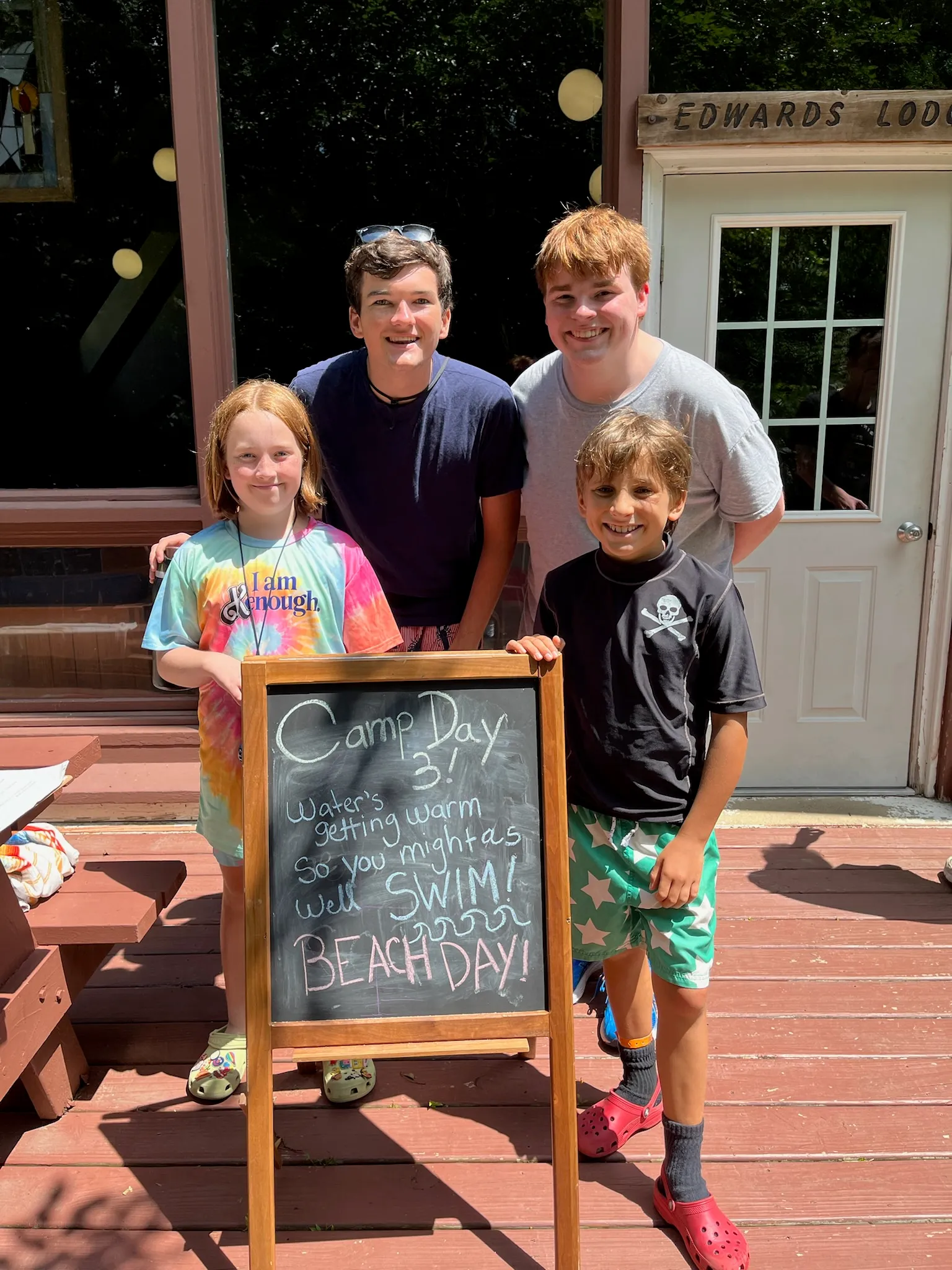 Kids posing with a chalkboard sign announcing beach day at camp